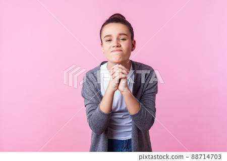 Please let me do this. Portrait of brunette teen girl with bun hairstyle in casual clothes holding hands in prayer, looking with imploring expression, begging permission. studio shot, pink background Please let me do this. Portrait of brunette teen girl with bun hairstyle in casual clothes holding hands in prayer, looking with imploring expression, begging permission. studio shot, pink background 88714703