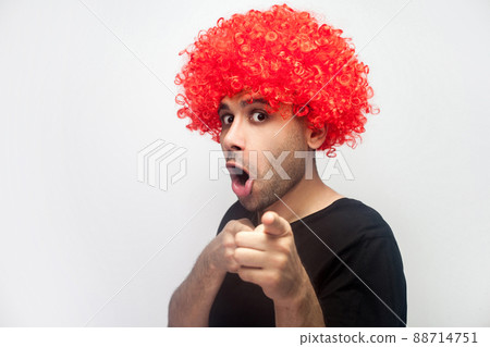 Portrait of funny surprised man with bristle and curly red wig pointing to camera and looking with shocked amazed hilarious face expression. indoor studio shot isolated on white background 88714751