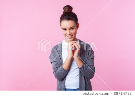 Portrait of funny playful brunette teenage girl with bun hairstyle in casual clothes grinning at camera with cunning sly expression, making tricky plan to prank friend. studio shot pink background Portrait of funny playful brunette teenage girl with bun hairstyle in casual clothes grinning at camera with cunning sly expression, making tricky plan to prank friend. studio shot pink background 88714752