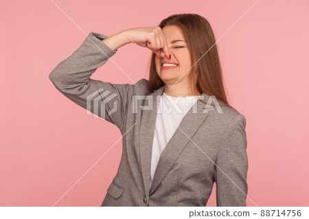 Bad smell. Portrait of young woman in business suit pinching nose and frowning in displeasure, expressing repulsion to stinky breath, awful odor, grimacing in disgust. indoor studio shot isolated Bad smell. Portrait of young woman in business suit pinching nose and frowning in displeasure, expressing repulsion to stinky breath, awful odor, grimacing in disgust. indoor studio shot isolated 88714756