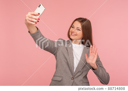 Portrait of charming businesswoman in suit jacket making video call with hello gesture, having online conference using cellphone, corporate cellular and mobile communication. studio shot isolated 88714808
