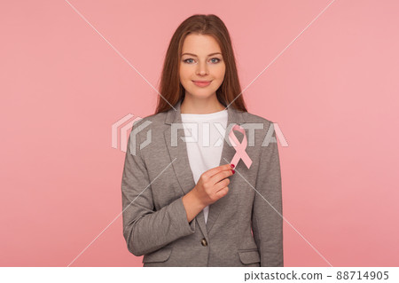 Female healthcare, medical insurance. Portrait of attractive positive businesswoman in elegant suit jacket holding pink ribbon, symbol of breast cancer awareness. indoor studio shot, pink background 88714905
