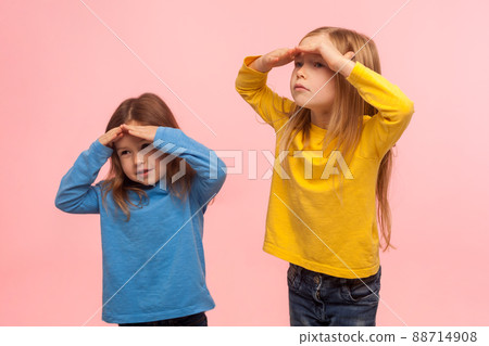 Portrait of funny amusing two little girls holding hands over eyes and looking far away with curious attentive expression, searching, viewing distance. indoor studio shot isolated on pink background Portrait of funny amusing two little girls holding hands over eyes and looking far away with curious attentive expression, searching, viewing distance. indoor studio shot isolated on pink background 88714908