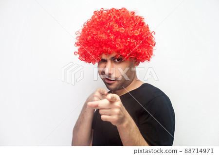 Portrait of funny positive man with bristle and red wig pointing to camera and winking playfully, flirting and getting acquaintance, asking for a date. studio shot, white background 88714971