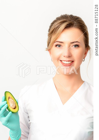 Portrait of smiling young female nutritionist doctor with organic avocado fruits posing at camera on white background, copy space. Benefits of proper nutrition Portrait of smiling young female nutritionist doctor with organic avocado fruits posing at camera on white background, copy space. Benefits of proper nutrition 88715128