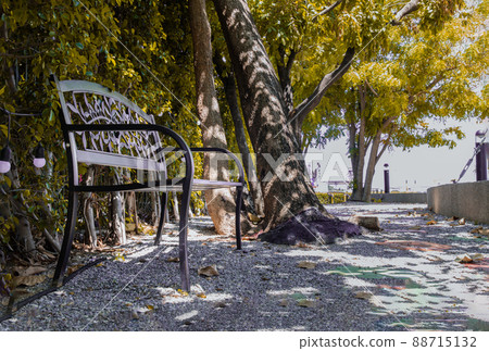Morning sunlight on backrest surface of Empty black wrought iron steel benched on the pebbles in a shady area of the quiet park area. Morning sunlight on backrest surface of Empty black wrought iron steel benched on the pebbles in a shady area of the quiet park area. 88715132