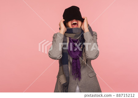 Portrait of angry mad girl in scarf pulling hat over her eyes and shouting, feeling crazy pissed off and desperate, autumn depression, nervous break down. studio shot isolated on pink background Portrait of angry mad girl in scarf pulling hat over her eyes and shouting, feeling crazy pissed off and desperate, autumn depression, nervous break down. studio shot isolated on pink background 88715212