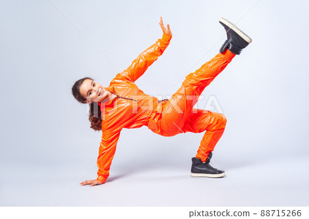 Full length image of vivid happy teenage girl with brunette hair wearing bright orange jumpsuit dancing hip-hop, showing move with handstand, hobby activities. studio shot isolated on white background Full length image of vivid happy teenage girl with brunette hair wearing bright orange jumpsuit dancing hip-hop, showing move with handstand, hobby activities. studio shot isolated on white background 88715266