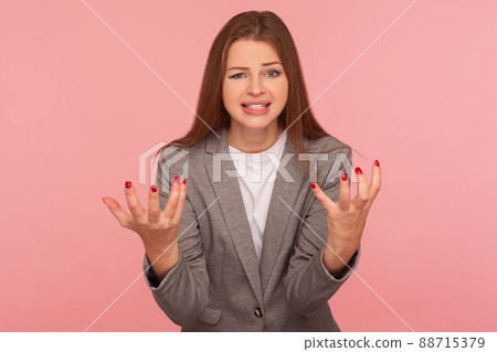 What do you want from me. Portrait of young mad woman in business suit raising hands and looking with anger hate, quarreling, annoyed by conflict. indoor studio shot isolated on pink background What do you want from me. Portrait of young mad woman in business suit raising hands and looking with anger hate, quarreling, annoyed by conflict. indoor studio shot isolated on pink background 88715379