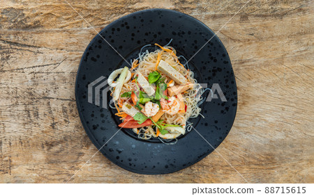 Top view of Seafood spicy glass noodle salad or Spicy delicious Mung bean Noodle Salad with fresh seafood (Yum woon sen) on wooden table. 88715615