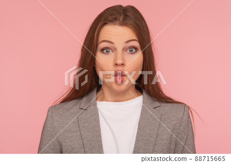 Closeup portrait of funny pretty young woman in business suit making fish face with pout lips, looking with humorous goofy grimace, comical amazement. indoor studio shot isolated on pink background Closeup portrait of funny pretty young woman in business suit making fish face with pout lips, looking with humorous goofy grimace, comical amazement. indoor studio shot isolated on pink background 88715665