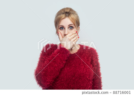 Portrait of shocked silence beautiful young blond woman in red blouse standing, covering her mouth and looking at camera with big eyes. indoor studio shot isolated on light gray background. Portrait of shocked silence beautiful young blond woman in red blouse standing, covering her mouth and looking at camera with big eyes. indoor studio shot isolated on light gray background. 88716001
