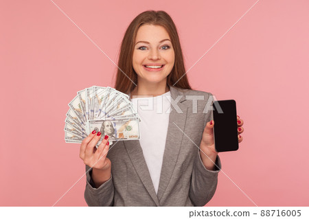 Apply online, loan application. Portrait of happy smiling businesswoman in suit jacket holding dollar banknotes and cellphone, satisfied with mobile banking. studio shot isolated on pink background Apply online, loan application. Portrait of happy smiling businesswoman in suit jacket holding dollar banknotes and cellphone, satisfied with mobile banking. studio shot isolated on pink background 88716005