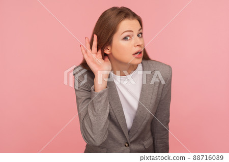 Portrait of curious nosy young woman in business suit holding hand near ear, listening carefully intently to interesting gossip, expressing amazement. indoor studio shot isolated on pink background 88716089
