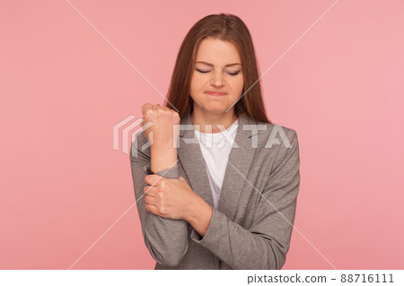 Injured hand, trauma. Portrait of unhealthy young woman in business suit feeling pain in wrist and grimacing, suffering carpal tunnel syndrome, pinched nerve. studio shot isolated on pink background 88716111