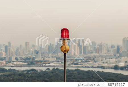 Red lantern of obstruction lights mounted on the rooftop of high rise tall building to ensure flights safety and warn the danger for the plane on the city view background. Red lantern of obstruction lights mounted on the rooftop of high rise tall building to ensure flights safety and warn the danger for the plane on the city view background. 88716217