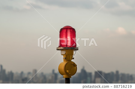Red lantern of obstruction lights mounted on the rooftop of high rise tall building to ensure flights safety and warn the danger for the plane on the city view background. Red lantern of obstruction lights mounted on the rooftop of high rise tall building to ensure flights safety and warn the danger for the plane on the city view background. 88716219