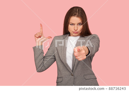 You are fired. Portrait of displeased young woman in business suit pointing to camera and making L sign with fingers, showing loser gesture, accusing for failure. studio shot, pink background 88716243