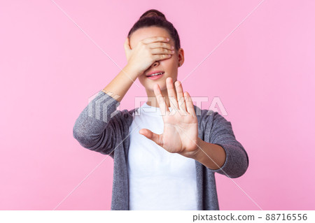 No, i don't want to look. Portrait of brunette teenage girl with bun hairstyle in casual clothes covering eyes and showing stop gesture, frightened or shocked of shameful content. indoor studio shot No, i don't want to look. Portrait of brunette teenage girl with bun hairstyle in casual clothes covering eyes and showing stop gesture, frightened or shocked of shameful content. indoor studio shot 88716556