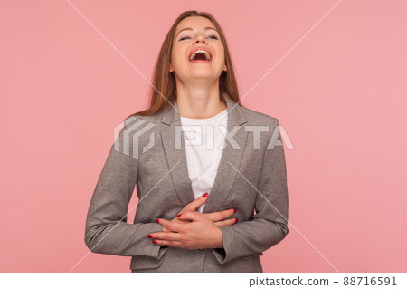 Portrait of happy carefree young woman in business suit holding her belly and laughing loud at joke, amused by funny anecdote, enjoying positive emotions. studio shot isolated on pink background 88716591