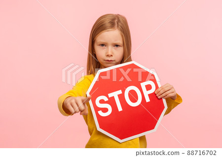 Portrait of cute serious bossy little girl holding Stop symbol, showing red traffic sign and pointing to camera, warning you about road safety rules. indoor studio shot isolated on pink background 88716702