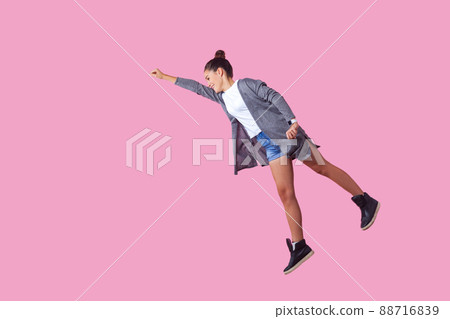 Superman. Portrait of cheerful ambitious brunette teenage girl with bun hairstyle in casual clothes flying with one raised hand, feeling super power. indoor studio shot isolated on pink background Superman. Portrait of cheerful ambitious brunette teenage girl with bun hairstyle in casual clothes flying with one raised hand, feeling super power. indoor studio shot isolated on pink background 88716839
