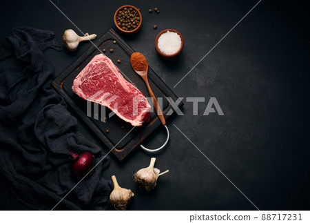 Raw juicy piece of beef meat on the bone lies on a wooden cutting board, spices for cooking on a black background. Meat tenderloin New York 88717231