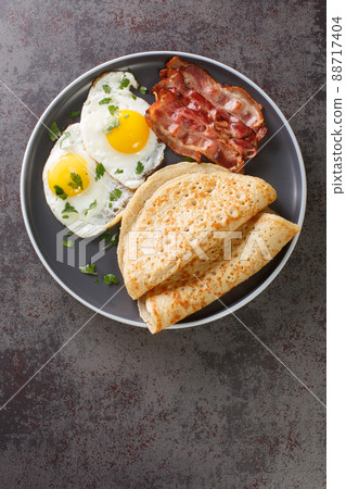English breakfast of bacon, eggs and oatcakes oat pancakes close-up in a plate. Vertical top view 88717404