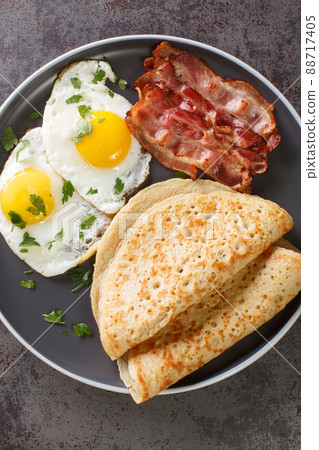 Traditional English Staffordshire oat pancakes, bacon and fried eggs close-up in a plate. Vertical top view 88717405