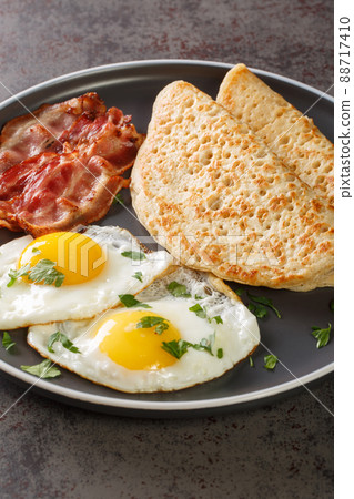 Traditional English Staffordshire oat pancakes, bacon and fried eggs close-up in a plate. Vertical Traditional English Staffordshire oat pancakes, bacon and fried eggs close-up in a plate. Vertical 88717410