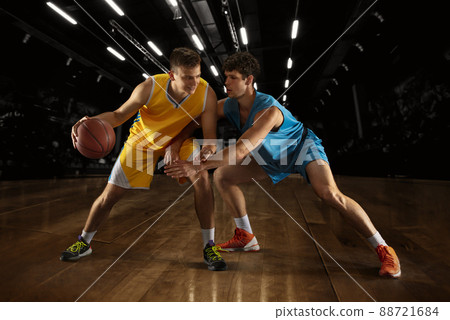 Poster with two young basketball players playing basketball in playground over dark background with flashlights. Concept of sport. Arena's drawned 88721684