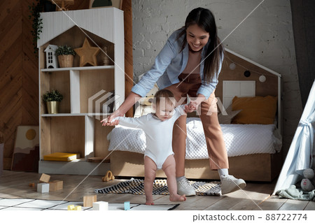Modern young woman spending free time at home teaching her playful baby daughter how to walk 88722774