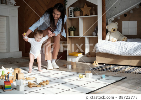 Cheerful young mother spending time at home teaching her lovely baby daughter how to walk 88722775