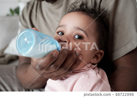 Close-up portrait of unrecognizable Black man bottle feeding his baby with formula or pumped breastmilk 88722898