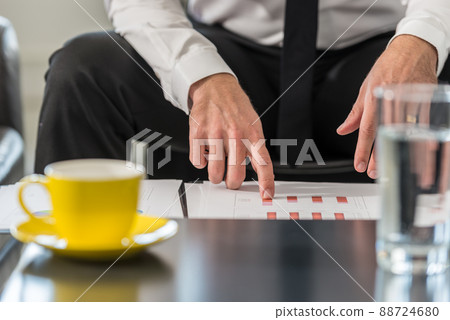 Businessman sitting at a club table in his office reviewing statistical charts Businessman sitting at a club table in his office reviewing statistical charts 88724680