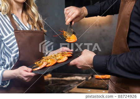 Close-up. a man and a woman in the kitchen are shifting tiger prawns onto a tray. 88724926
