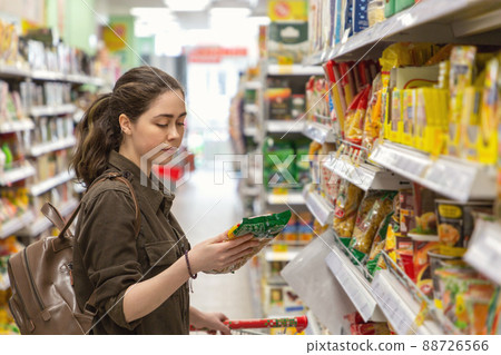 Portrait of a young pretty woman carefully chooses the products in the store. Concept of consumerism Portrait of a young pretty woman carefully chooses the products in the store. Concept of consumerism 88726566