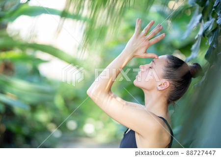 Female meditating and practicing yoga in tropical rainforest. Beautiful young woman practicing yoga outdoor with tropical forest in background. 88727447