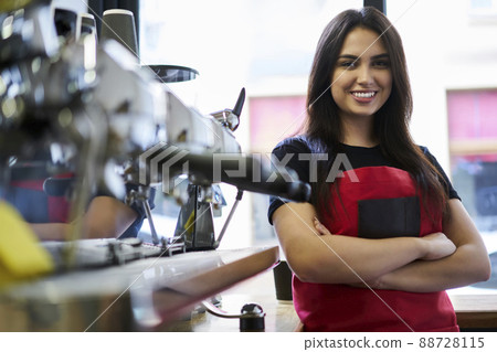 Happy female barista with crossed hands near professional machine at bar in cafeteria Happy female barista with crossed hands near professional machine at bar in cafeteria 88728115