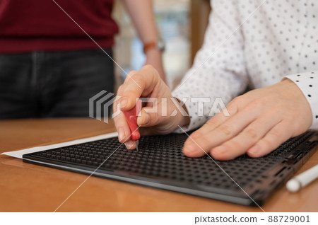 A man teaches a woman how to use a special stencil and stylus to write a letter in Braille. A man teaches a woman how to use a special stencil and stylus to write a letter in Braille. 88729001