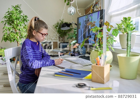 Girl child sitting at home at table with computer listening online lesson 88729031