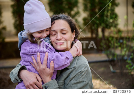 Beautiful woman mother hugging her lovely daughter while standing together in the backyard of her country house on an early spring day. Family relationships, Mother and Children protection Day 88730876