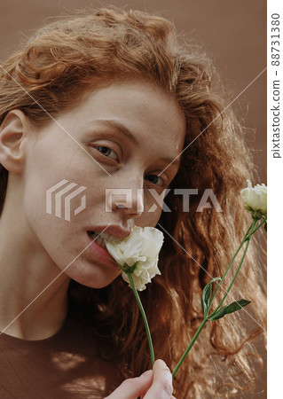Portrait of ginger girl with natural beauty looking at camera and biting white flower 88731380