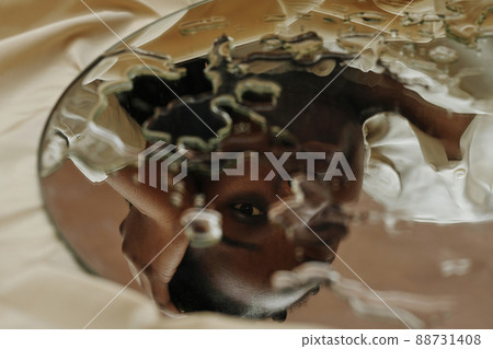 Close-up of reflection of young African woman looking through drops in mirror Close-up of reflection of young African woman looking through drops in mirror 88731408