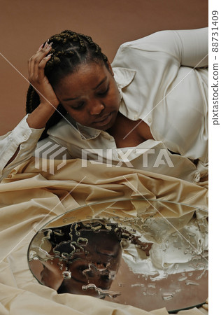African plump woman lying and looking at her reflection in mirror with drops on it 88731409