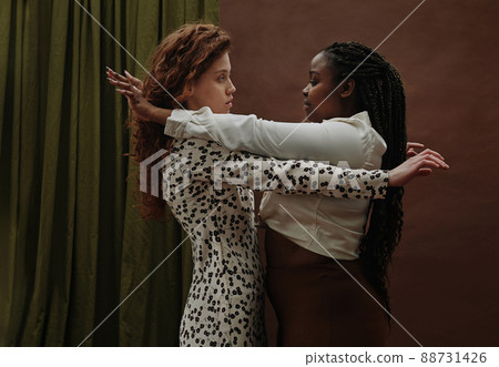 Two young girls in different nationality embracing each other standing against the brown background Two young girls in different nationality embracing each other standing against the brown background 88731426