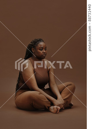 Portrait of young black woman in casual clothing sitting with blank expression isolated on brown background 88731440