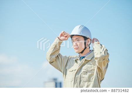 A young man in work clothes wearing a helmet against the blue sky 88731482