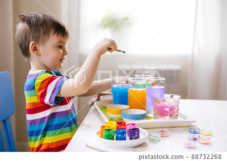 Cute baby boy learning mixing different colors with water and paint in containers. Early development Cute baby boy learning mixing different colors with water and paint in containers. Early development 88732268