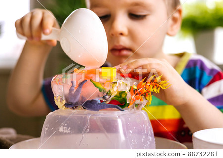 A cute little child pours warm water over toys frozen in ice. Dinosaur defrosting. Early development 88732281